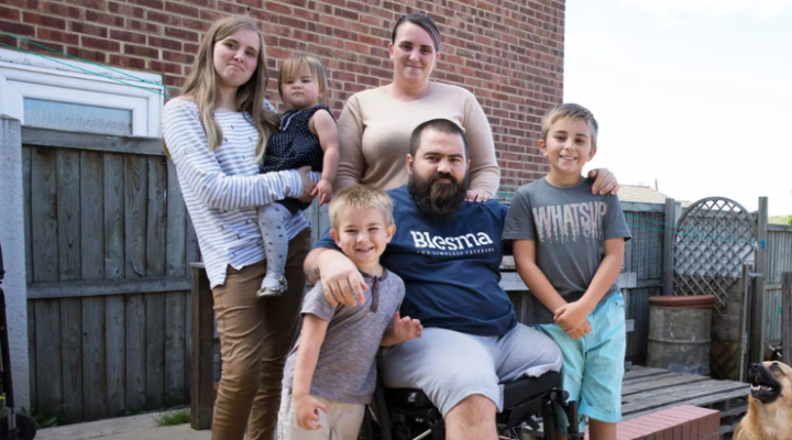 Lionel, a Blesma member, seated in a wheelchair surrounded by his family outside their home