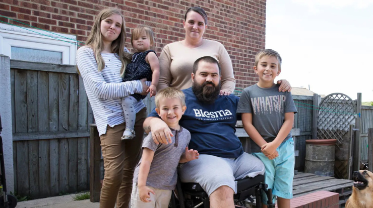 Lionel, a Blesma member, seated in a wheelchair surrounded by his family outside their home