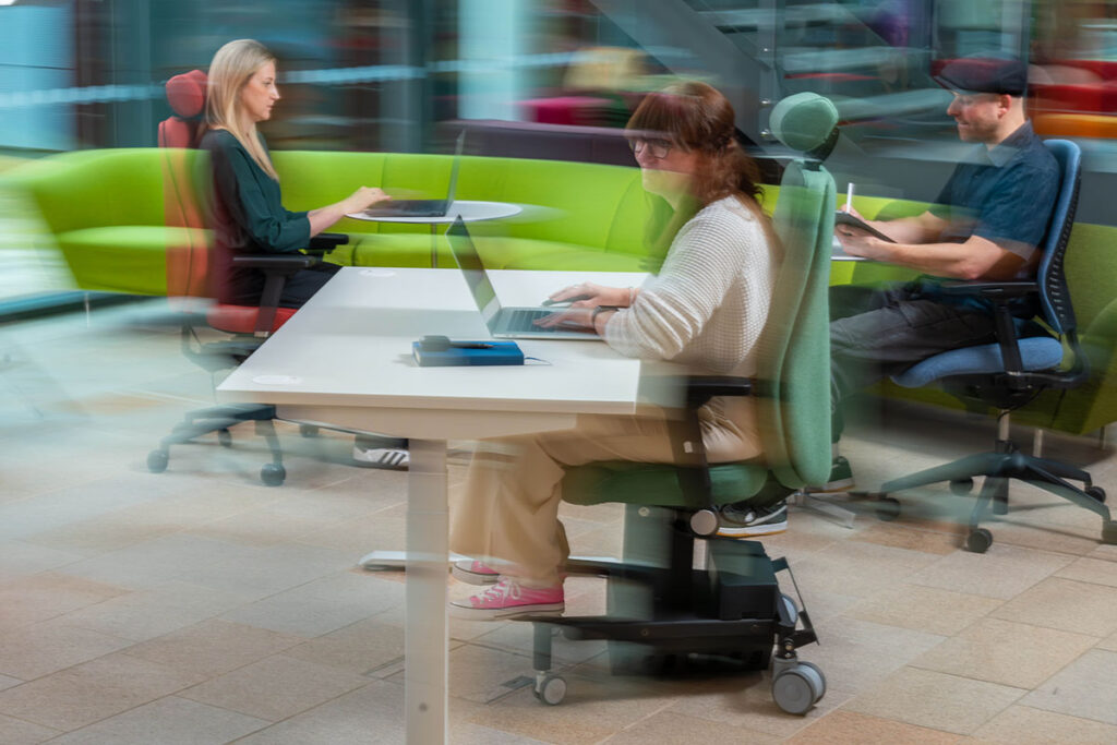 Three people working in Ergochair ergonomic chairs in a busy open-plan office environment