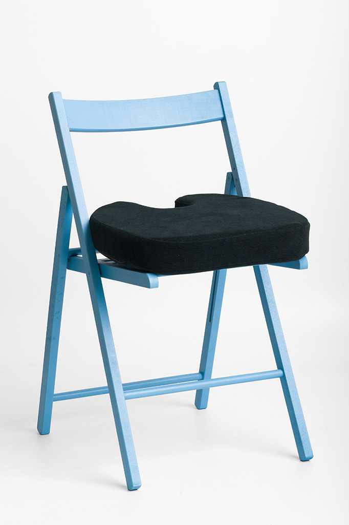 Actyv coccyx wedge cushion with cut-out placed on a blue folding chair