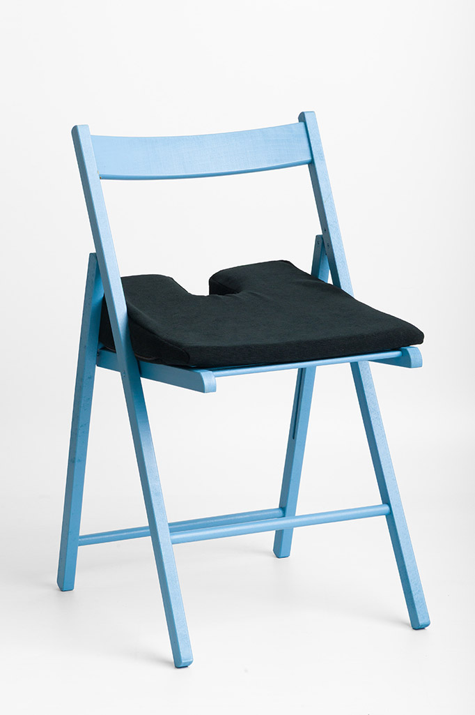 Actyv coccyx cushion with cut-out placed on a blue folding chair