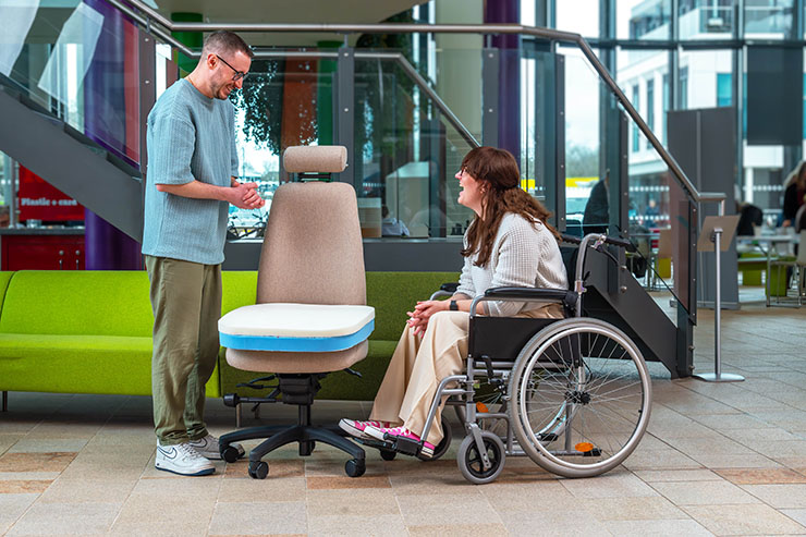Ergochair assessor discussing ergonomic chair options with a wheelchair user in a modern office environment