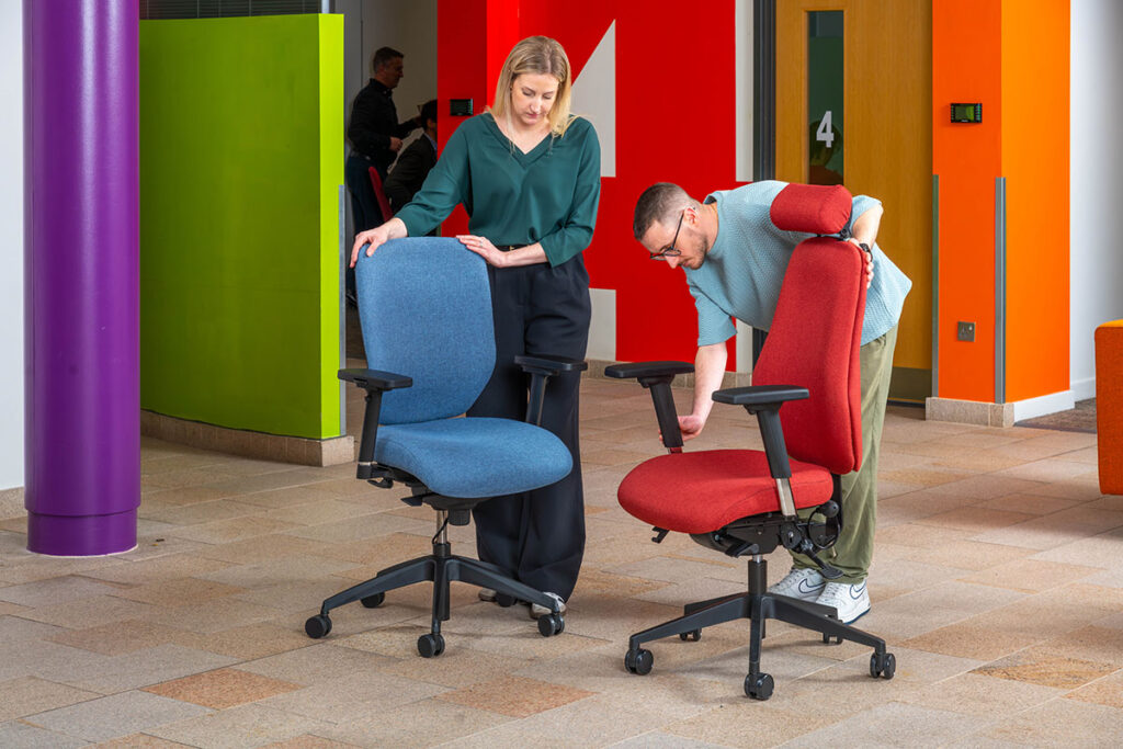 Two Ergochair team members examining ergonomic chairs in blue and red upholstery in a colourful office space